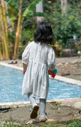 A vertical shot of a young girl walking around a shallow water pool in a garden