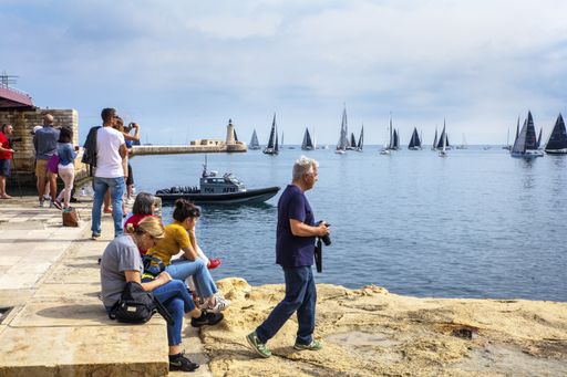 Spectators watching and photographing the Rolex Middle Sea Yacht Race from shore of Grand Harbour, Malta, Mediterranean