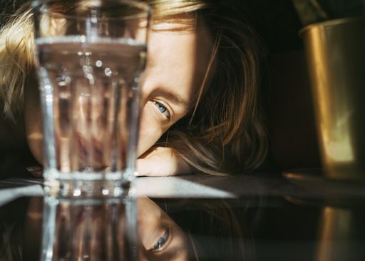 A shallow focus of a blonde female with blue eyes lying on the table with a glass of water on it