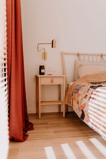 A modern bedroom interior with a bed and night stand situated in front of red curtains