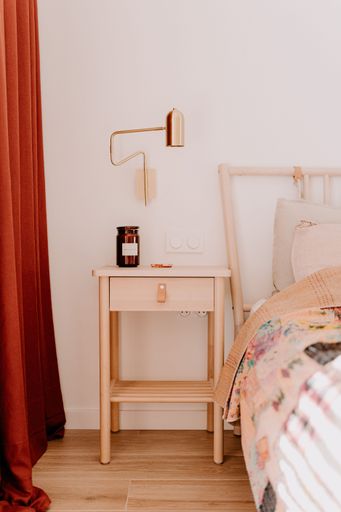 A modern bedroom interior with a bed and night stand situated in front of red curtains