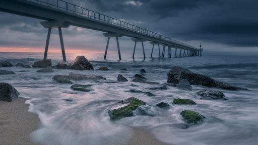 An amazing shot of a sandy and rocky beach with modern pier on a sunset background