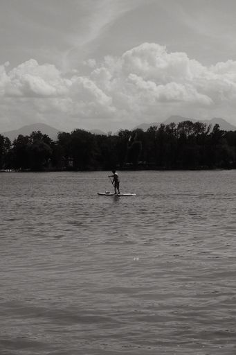 A grayscale shot of a man paddleboarding on Chiemsee lake in Bavaria, Germany on a sunny day