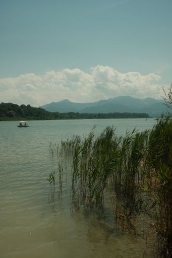 A gorgeous view of the Chiemsee in Bavaria, Germany with a tiny boat sailing across it under a cloudy sky