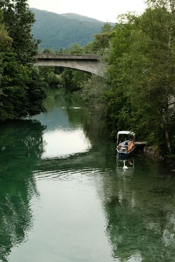A small boat surrounded by lovely green trees at the Mangfall River with a bridge over it in Gmund am Tegernsee, Germany