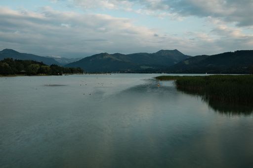 A gorgeous view of the Tegernsee in Bavaria, Germany with tall green hills reflected in it under a cloudy sky