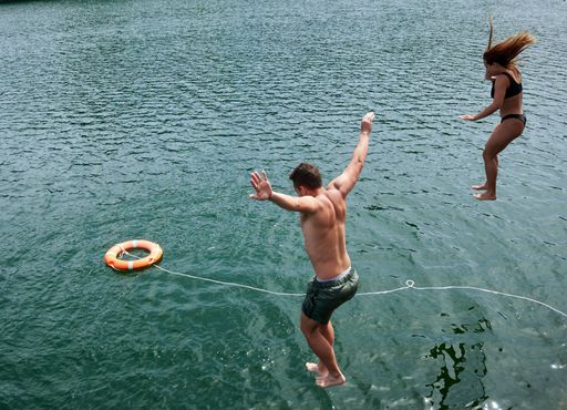 The young Hispanic man and woman jumping in sea water with orange safety ring floating on the surface