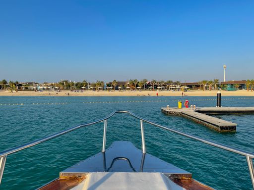 A serene view of the sandy beach, calm blue sea and pier, visible from the ship in daylight