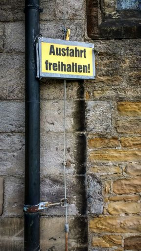 A vertical shot of an old brick wall with an external old steel pipe and a yellow sign