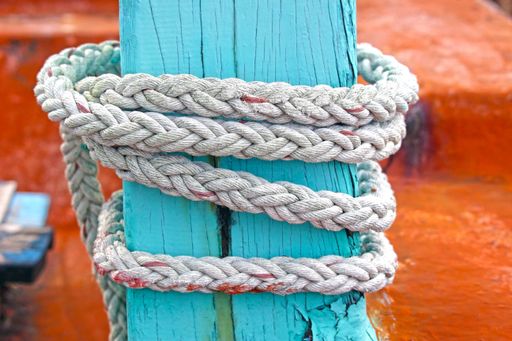 Close-up of a dock line rope secured to a colorful turquoise old wooden piling on a boat