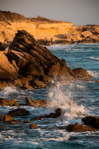 A vertical shot of sea waves crashing into the rock formations near the shore