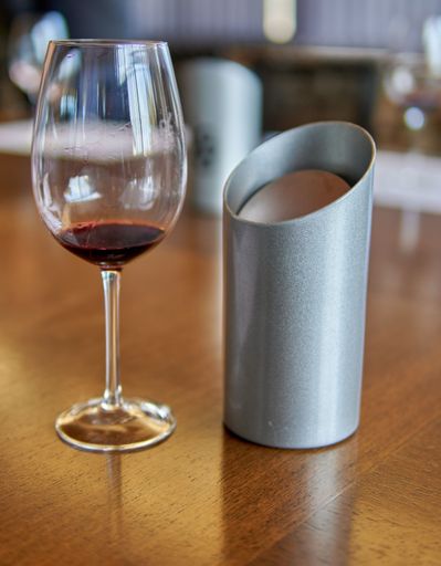 A vertical shot of a wineglass and a metal spittoon at a wine tasting