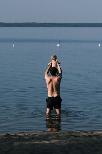 A vertical shot of a Caucasian father holding his kid high above the water of the sea