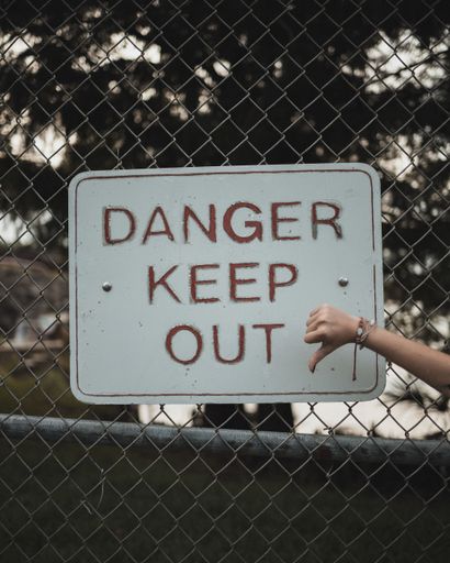 A vertical closeup of a tablet on a mesh fence with "danger keep out" with a holding thumb down