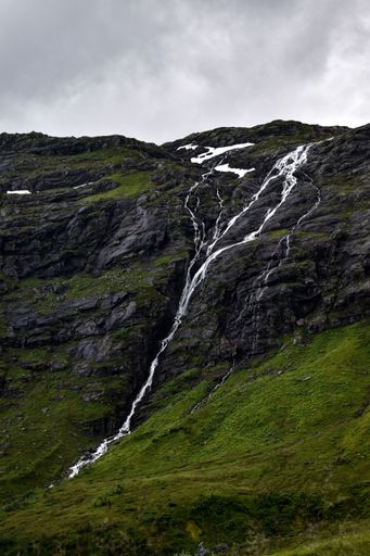 A vertical shot of a waterfall falling down the mossy rocks under a gray cloudy sky