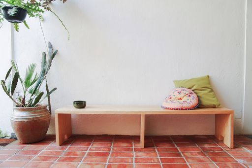 A wooden bench with cushions against a white wall