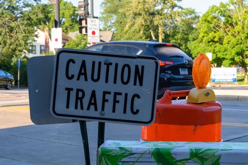 Caution Traffic sign downtown city crosswalk on a summer, sunny morning, with a car in the background, trees and construction light.