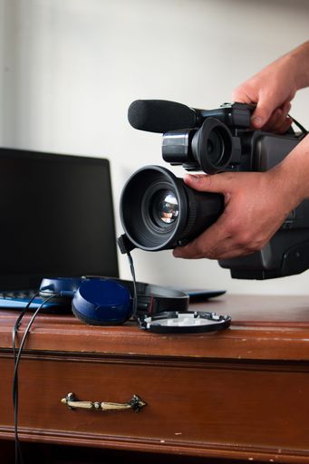 A closeup of a pro camera held above a wooden desk with a laptop in the background