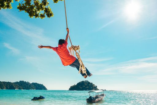 The young boy swinging on the rope against the background of the sea. Childhood, carefree, happy.