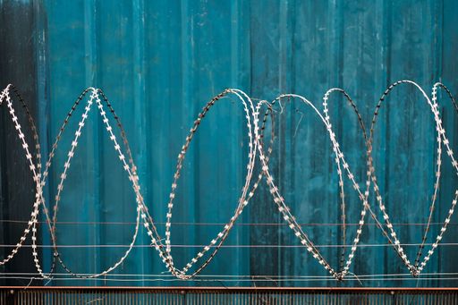 A closeup of metal barbed wire fences in background of blue wall