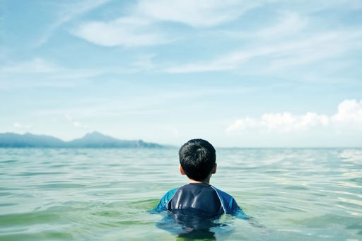 A back view of boy swimming in sea in background of blue sky