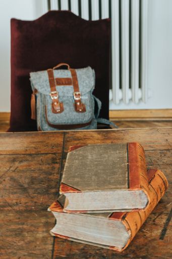 A closeup of old books on wooden table in background of bag on chair