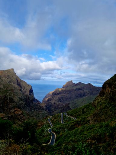 A narrow path going around green hills in the wilderness under a beautiful cloudy sky on a sunny day