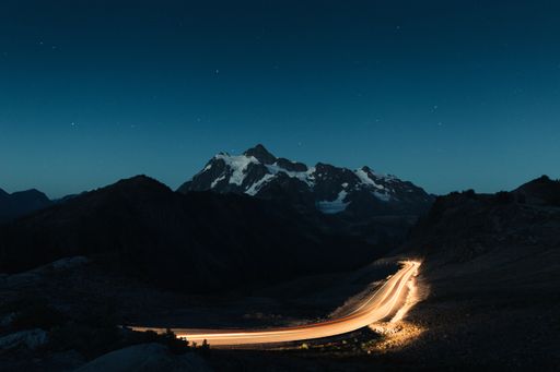 Amazing night sky full of stars with snowy rocky mountains in the middle and a dimly lit road. Beautiful Landscape