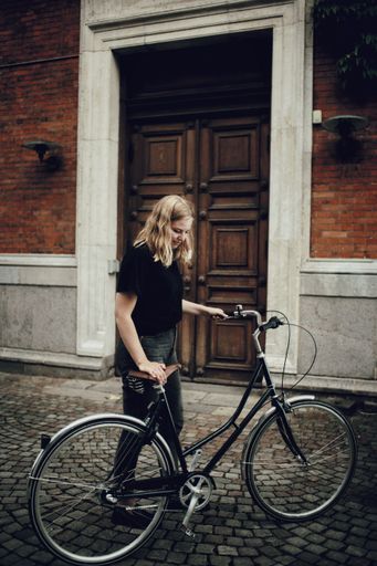 A vertical shot of blonde Caucasian woman standing by a bicycle in a street in Copenhagen, Denmark