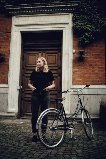 A vertical shot of blonde Caucasian woman standing by a bicycle in a street in Copenhagen, Denmark