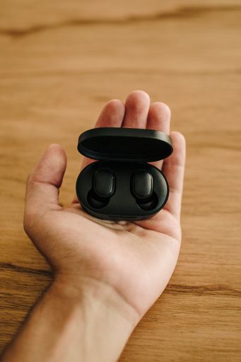 A vertical shot of a person holding black wireless earbuds on a wooden table