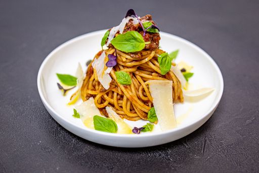 A close-up of spaghetti bolognese on a black table served with herbs