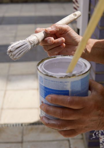 A vertical shot of a person holding a pail with white paint and a brush