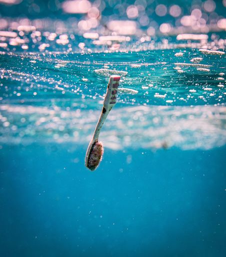 A closeup of a dirty toothbrush in the blue ocean water - pollution