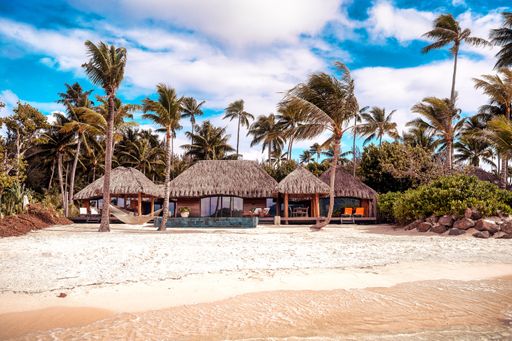 The Thatched buildings on a beach surrounded by palm trees on a beautiful sunny day in Bora Bora