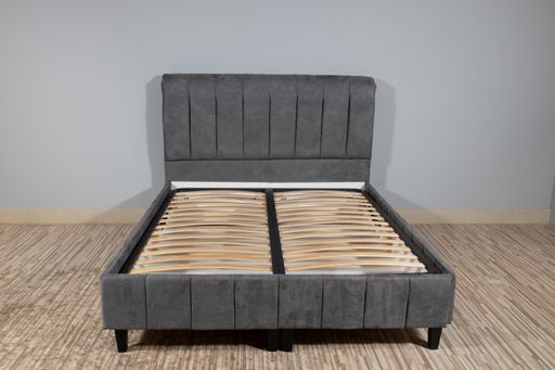 A bed with gray upholstery without mattress in an empty room