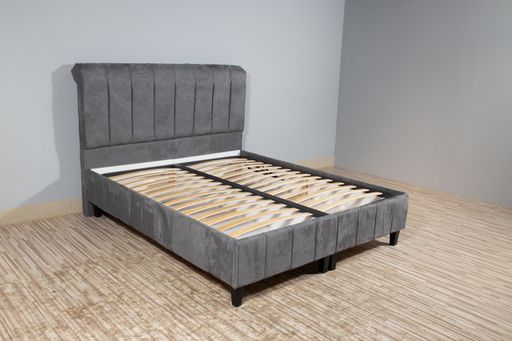 A bed with gray upholstery without mattress in an empty room