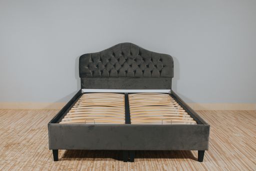 A bed with gray upholstery and without mattress in an empty room