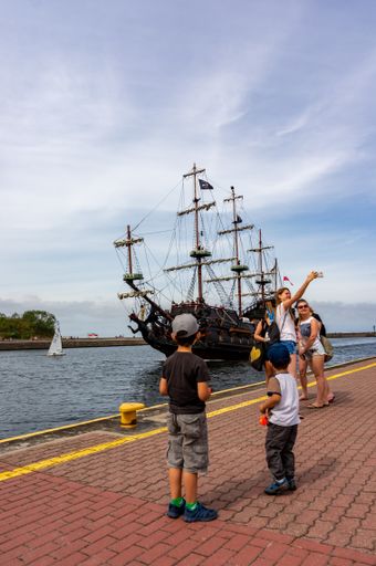 Two young boys standing on a pier close by a wooden pirate ship