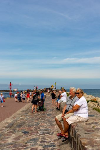 People sitting on a small wall along a pier next to the beach on a cloudy day.