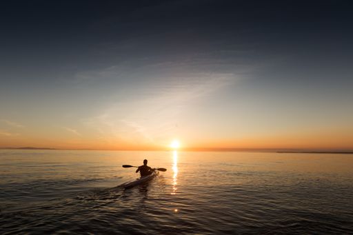 A man in a rowboat going towards the sunrise in a beautiful sea with sunlight shining on the horizon