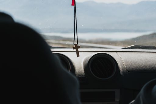 A Christian cross hanging in front of the front window of a car