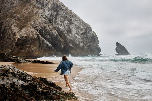 A female in blue shorts walking on the wet sand washed by the waters of the turbulent sea