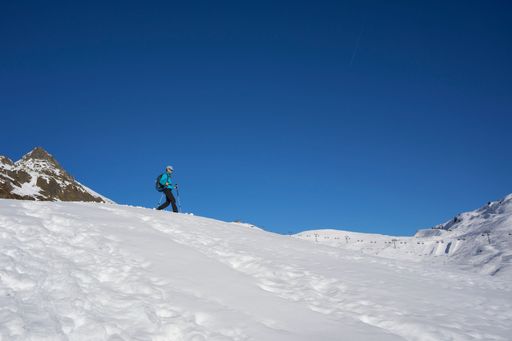A female hiker with walking sticks on a snowy mountain under a clear cloudless sky
