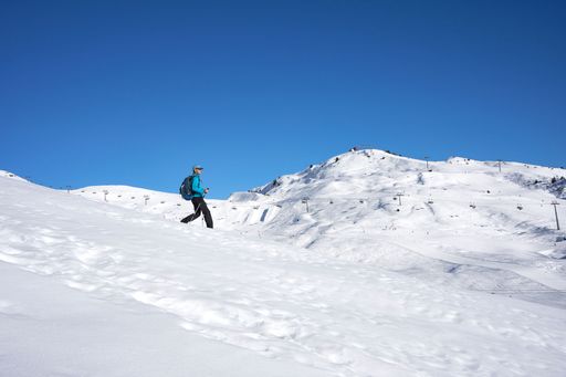 A female hiker with walking sticks on a snowy mountain under a clear cloudless sky