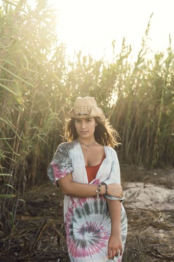 A vertical shot of a beautiful female smiling and holding her hat during a windy day