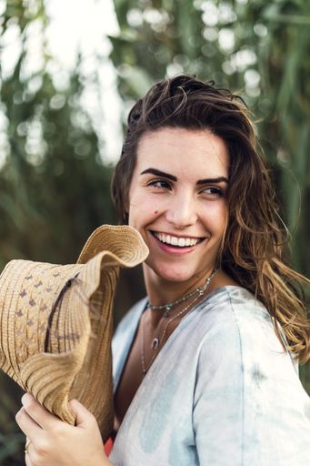 A vertical shot of a beautiful female smiling and holding her hat during a windy day