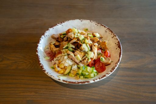 A closeup shot of a chicken bowl with veggies on the wooden background