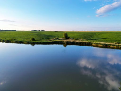 A beautiful view of the lake near the green field and the sky with clouds reflecting in the water