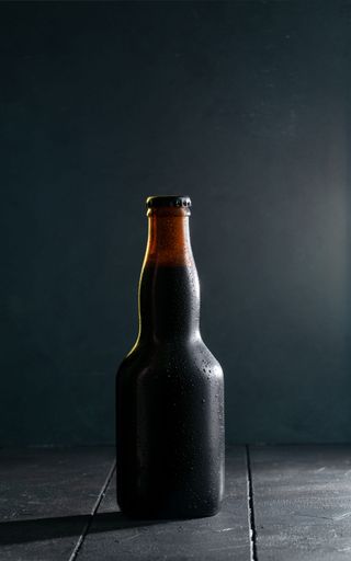 A vertical closeup shot of a brown glass beer bottle on a wooden table with a black background